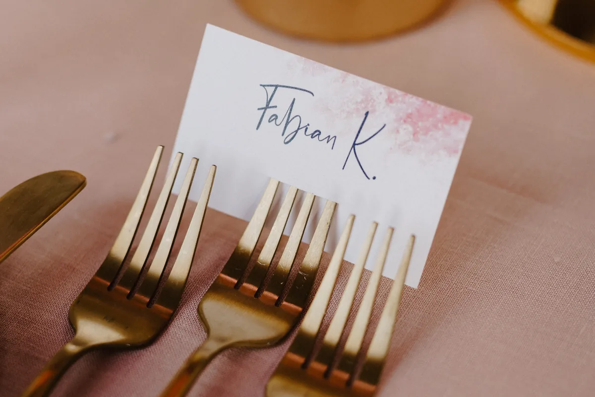 Platzkarte mit Kalligrafie zwischen goldenem Besteck