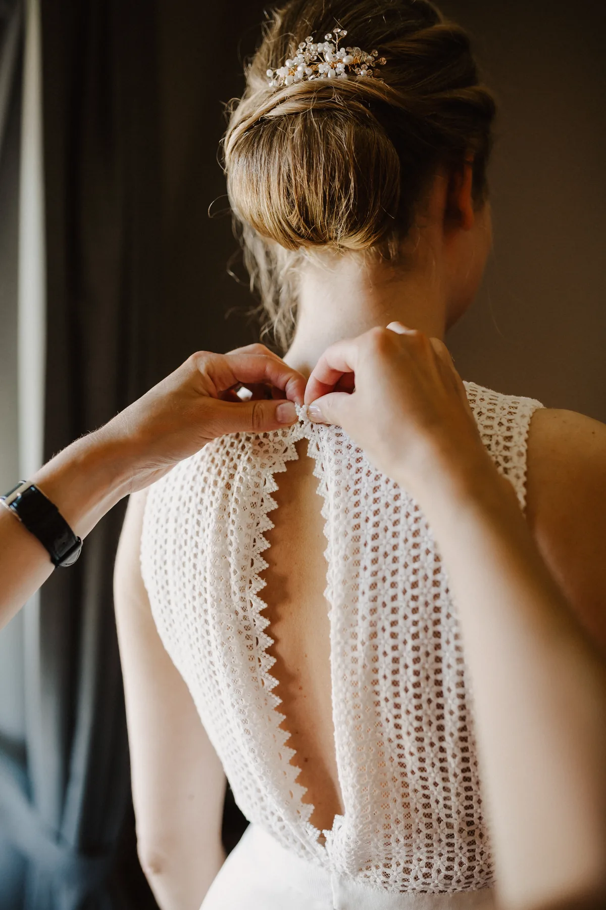 Braut beim Getting Ready, Spitzenrücken des Brautkleids wird geschlossen