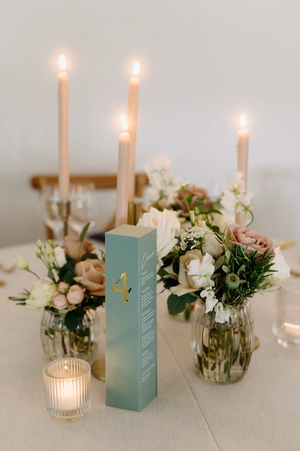 Tischaufsteller in Petrol mit goldenem Motiv zwischen Kerzen und Blumen