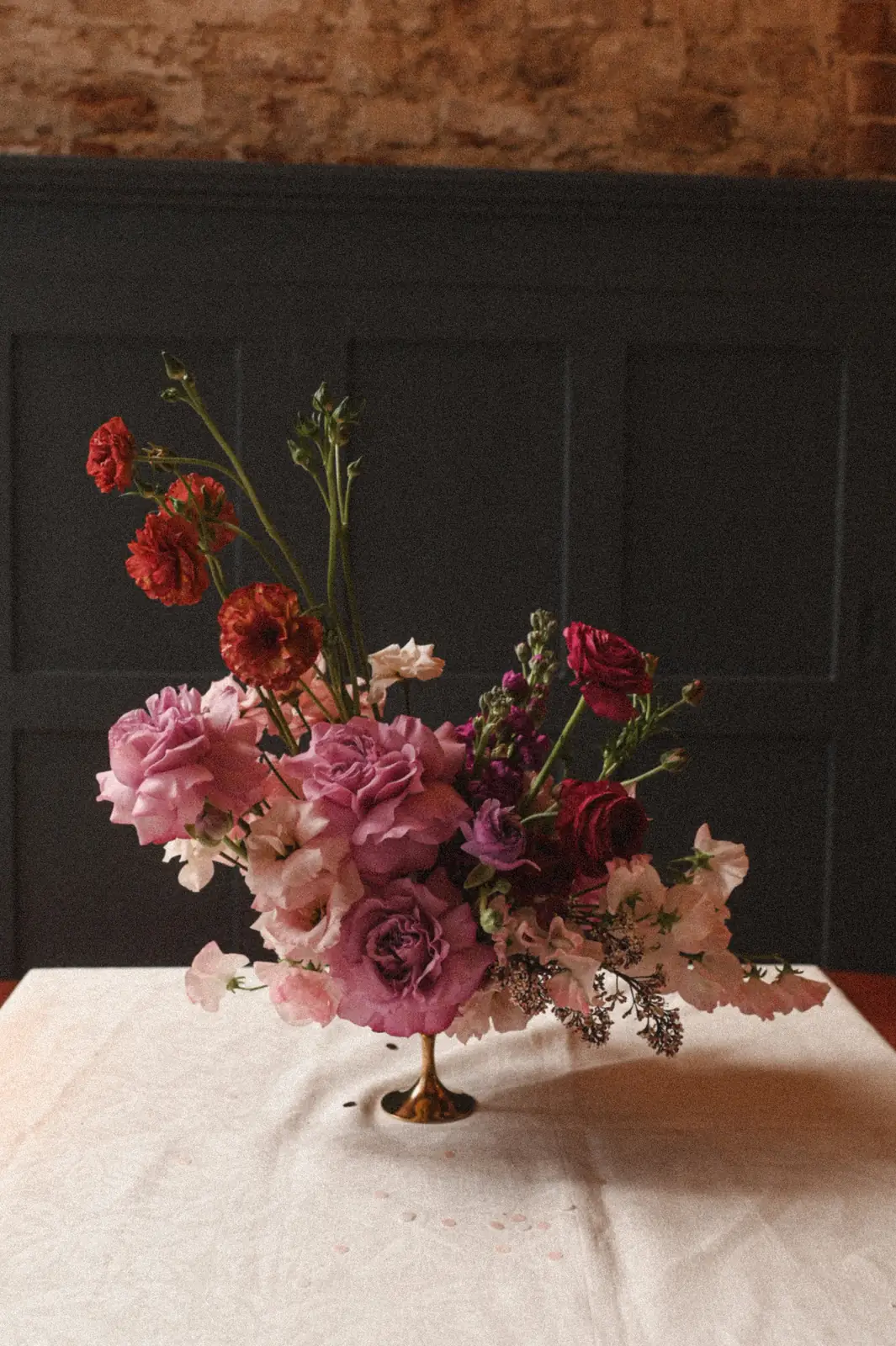 Blumengesteck in Rosa, Pink und Rot in einer goldenen Schale vor dunkler Wandvertäfelung