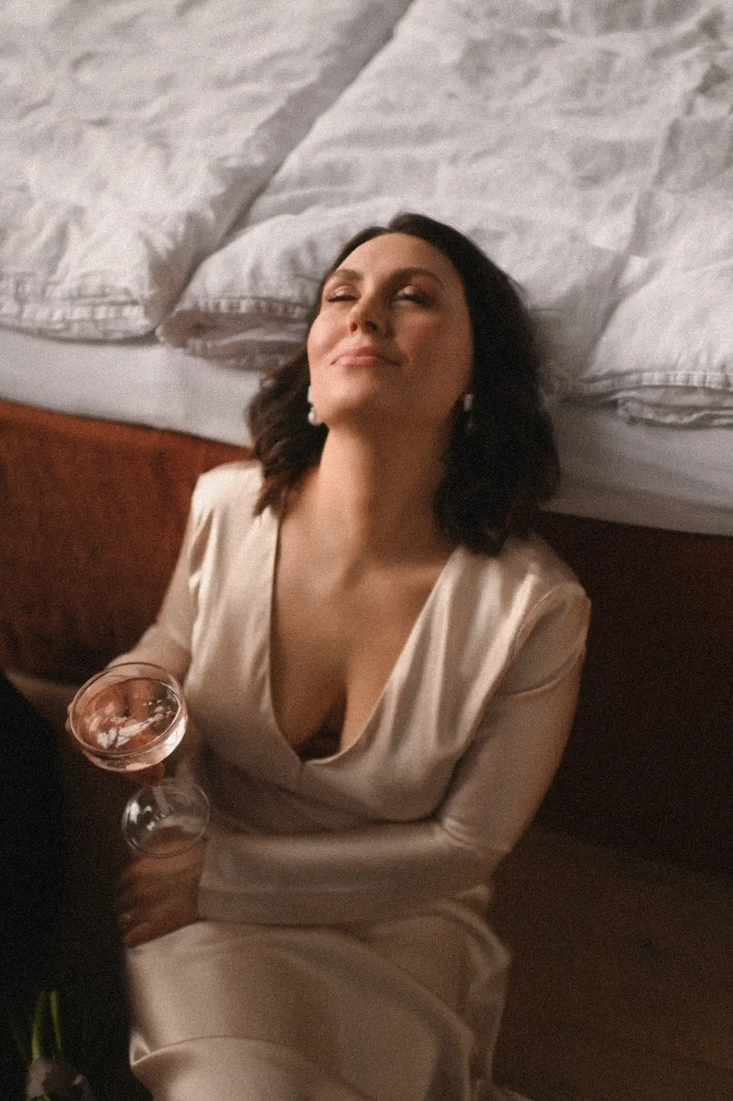 Die Braut lehnt entspannt am Bett, mit einem Glas Rosé in der Hand