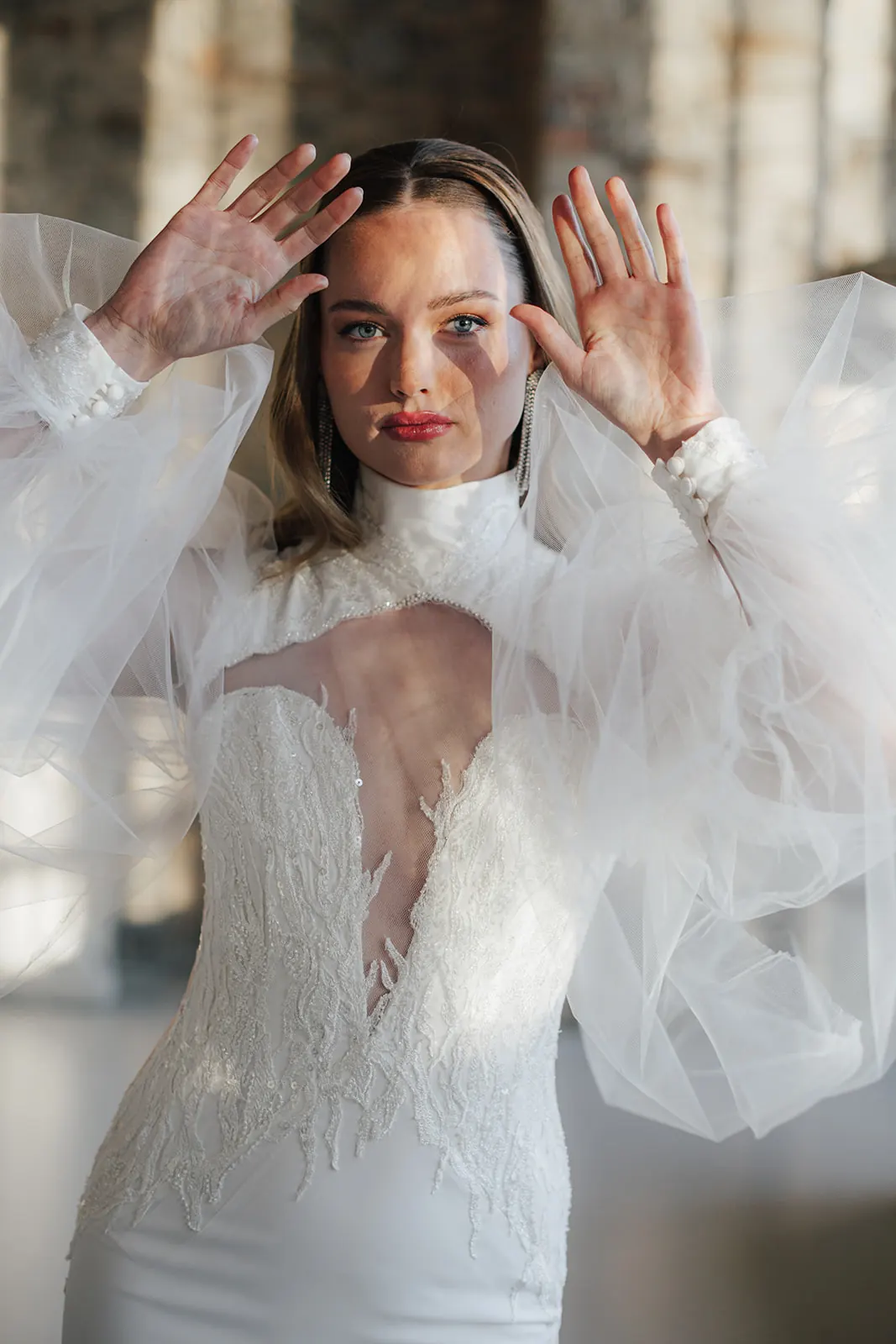 Die Braut im Kleid mit Tüllärmeln hebt die Hände ans Gesicht