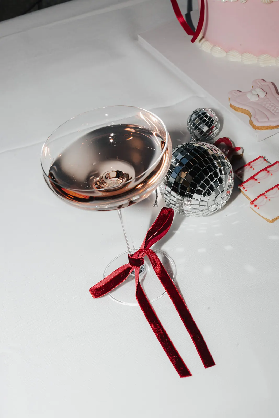 Sektschale mit roter Samtschleife neben Discokugeln und verzierten Keksen