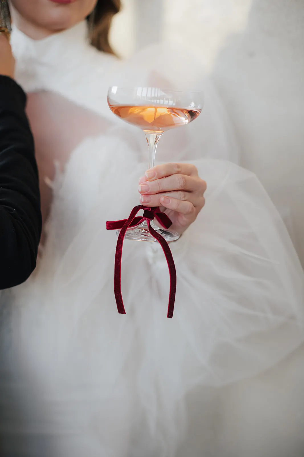 Die Braut hält ein Glas Rosé mit weinroter Samtschleife am Stiel