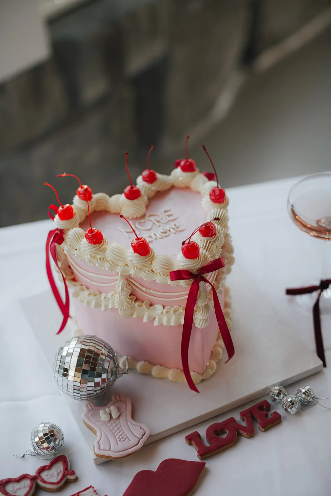 Torte in Herzform in Rosa mit Sahnetupfen, Kirschen und roten Schleifen